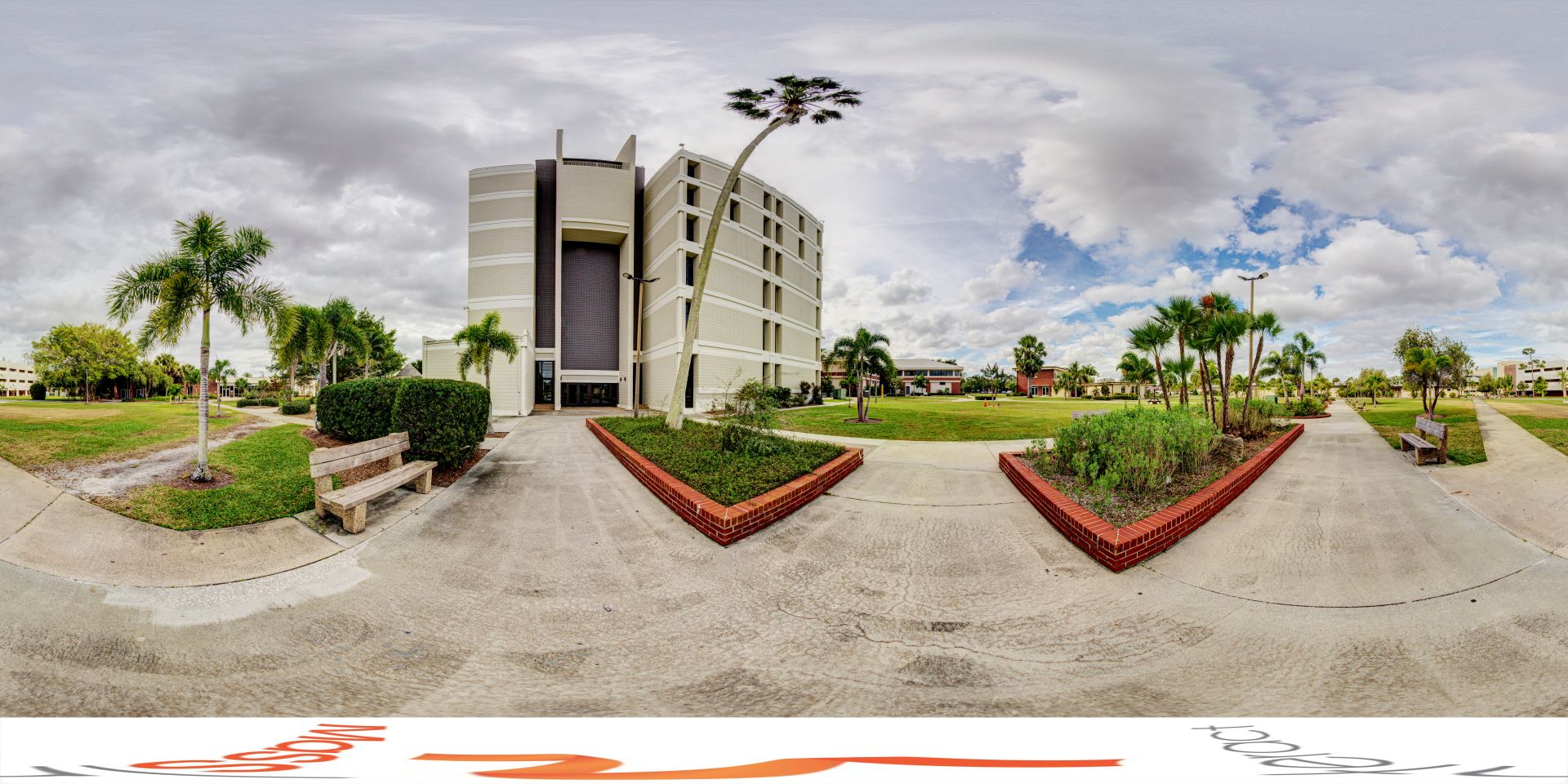 Panoramic view of a university campus featuring the Crawford building, a tall white structure, surrounded by lush green lawns and palm trees under a cloudy sky